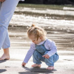 Three year old girl plays in the sand at the beach with her mum